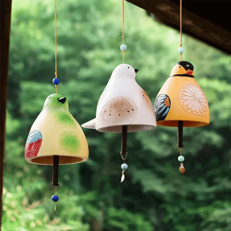 Drei BirdChime Windspiele in Grün, Weiß und Gelb hängen unter einem Vordach im Garten