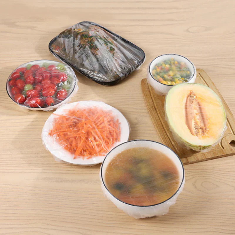 Mehrere mit PlasticWrap abgedeckte Schüsseln mit Erdbeeren, Karotten, Melone und Suppe
