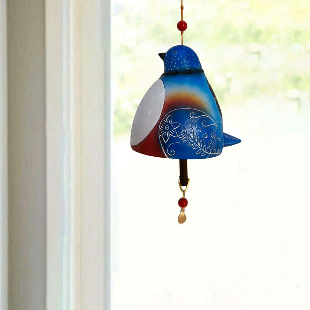 Blaues BirdChime Windspiel im Blauvogel-Design hängt vor einem Fenster mit Gartenblick