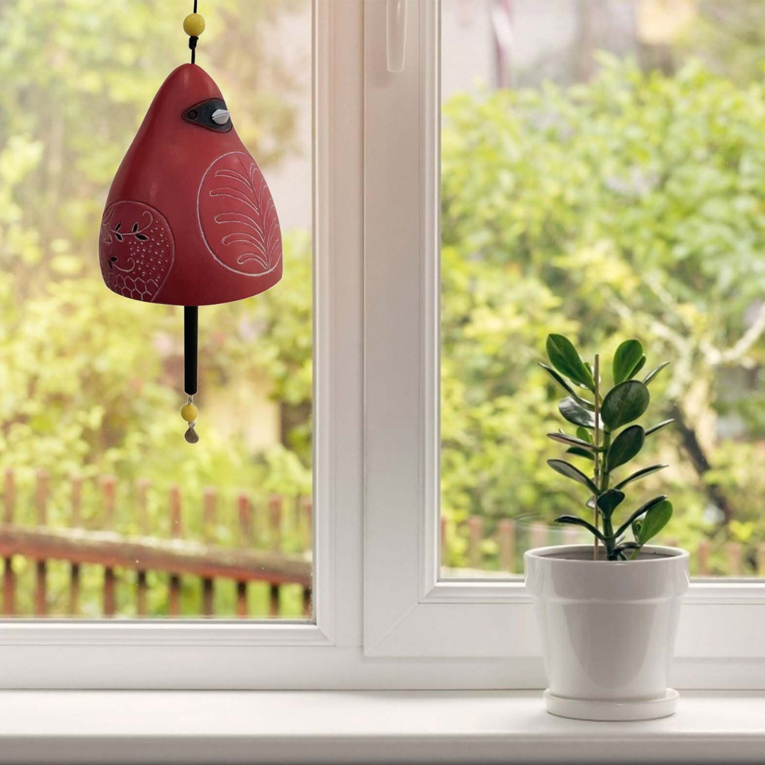 Rotes BirdChime Windspiel im Kardinal-Design hängt an einem Fenster mit Zimmerpflanze im Hintergrund