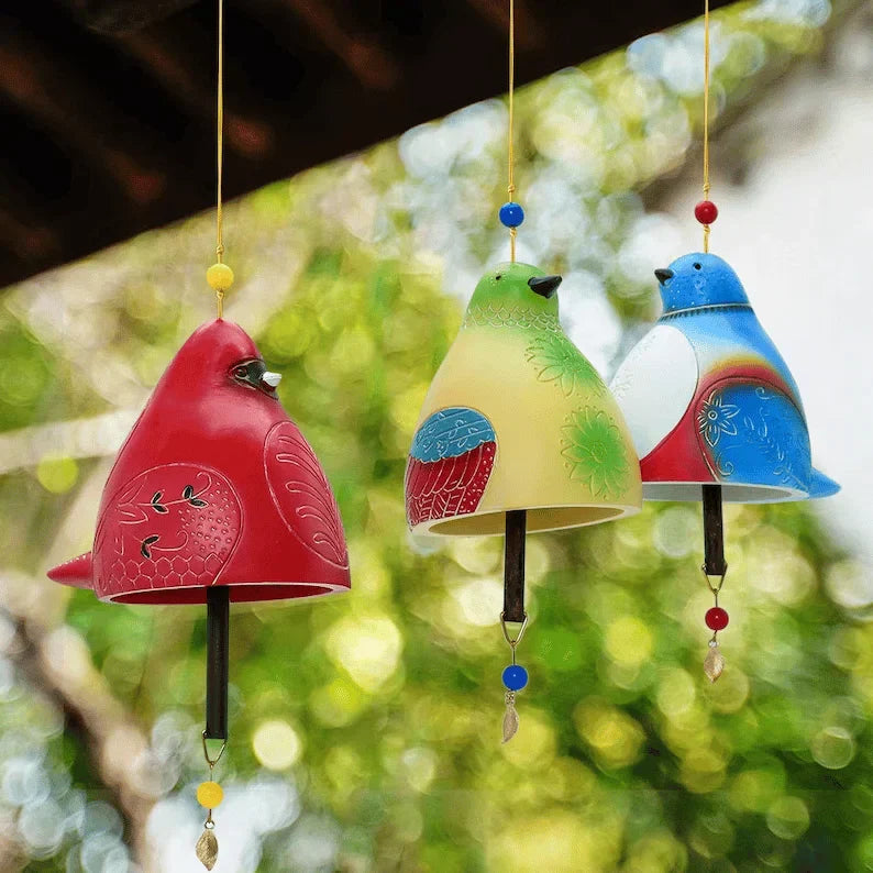 Drei BirdChime Windspiele in Rot, Grün und Blau hängen im Freien vor grünem Hintergrund